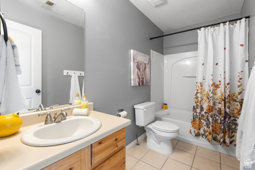 Full bathroom with tile patterned floors, shower / bathtub combination with curtain, toilet, vanity, and a textured ceiling