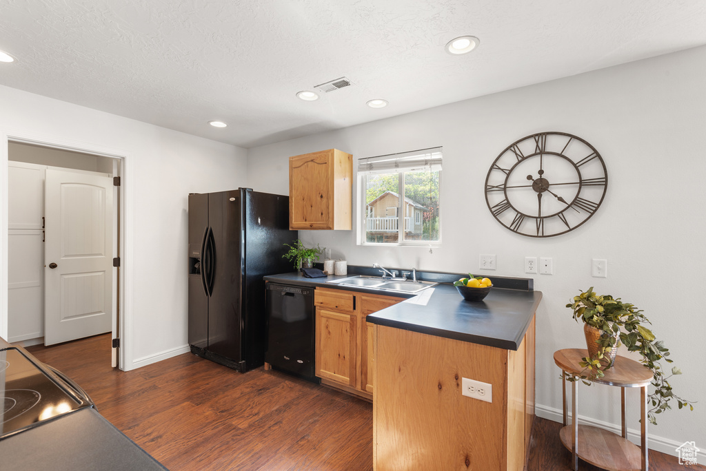 Kitchen with black appliances, a sink, dark countertops, dark wood-type flooring, and baseboards