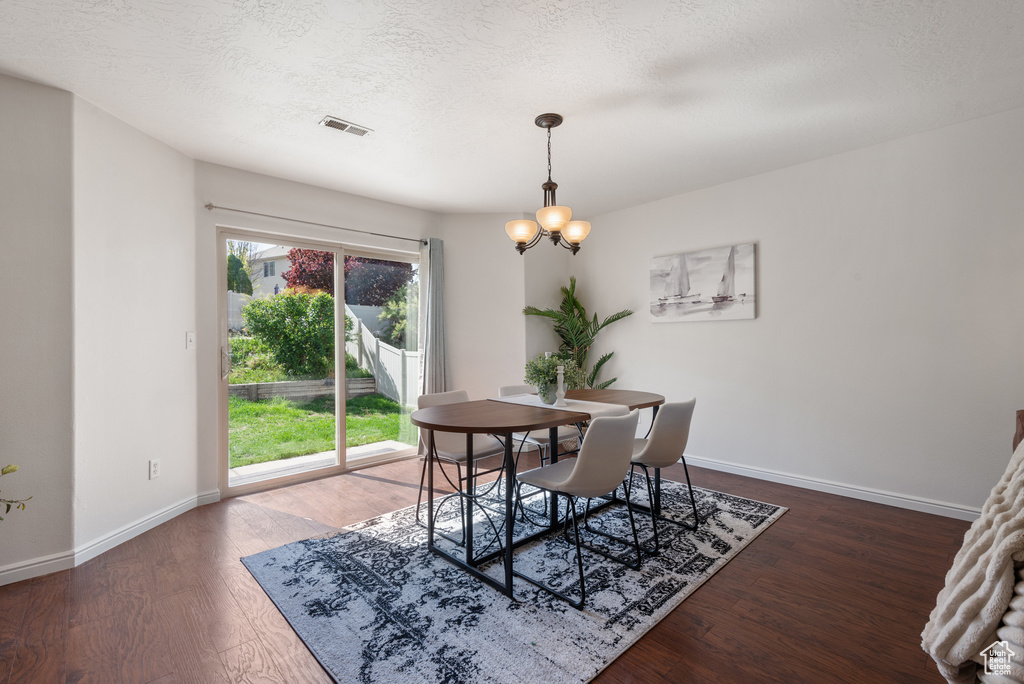 Dining space featuring wood finished floors, baseboards, a chandelier, and a textured ceiling