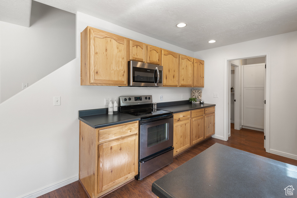 Kitchen with appliances with stainless steel finishes, dark wood-style floors, dark countertops, and recessed lighting