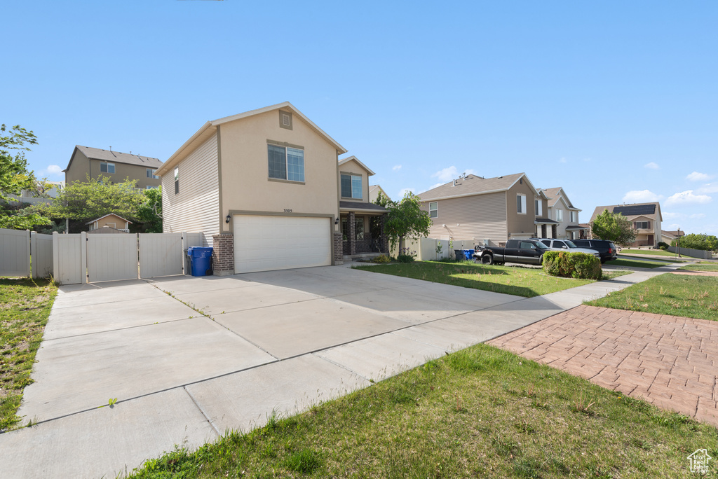 View of front of house featuring concrete driveway, a gate, an attached garage, a residential view, and brick siding