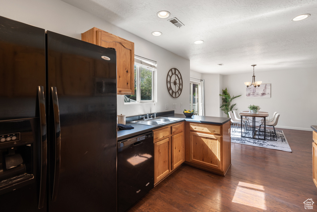 Kitchen with black appliances, a sink, a peninsula, dark wood finished floors, and dark countertops