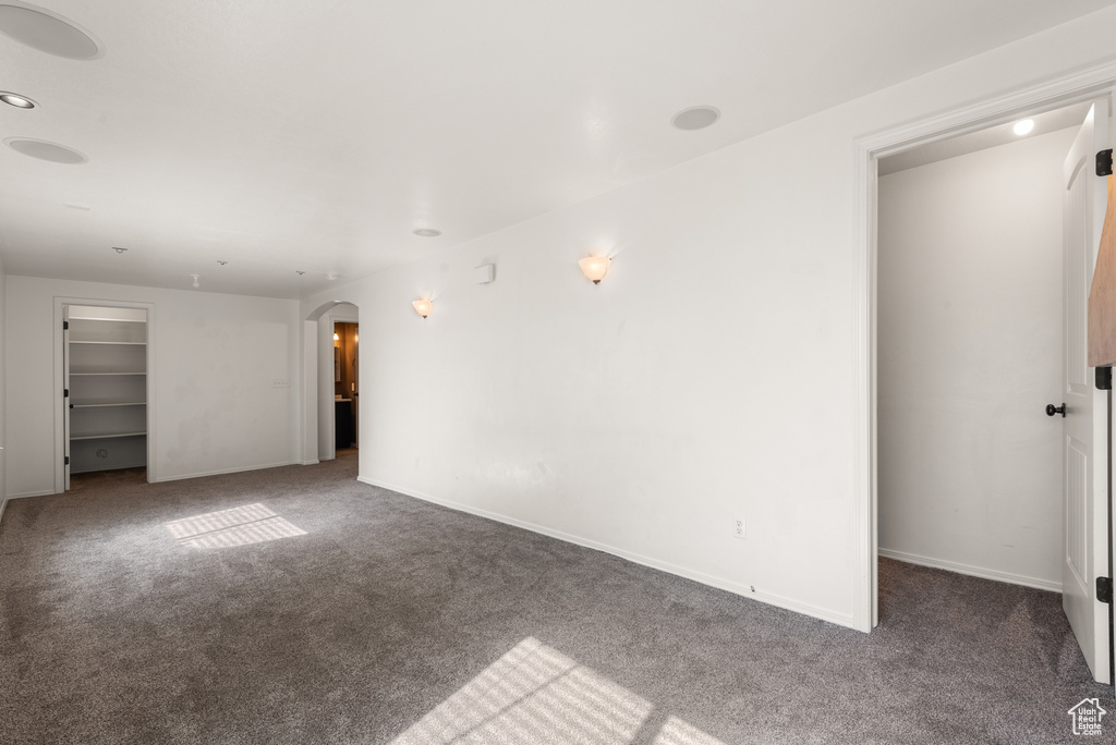 Unfurnished living room with arched walkways, carpet flooring, and baseboards