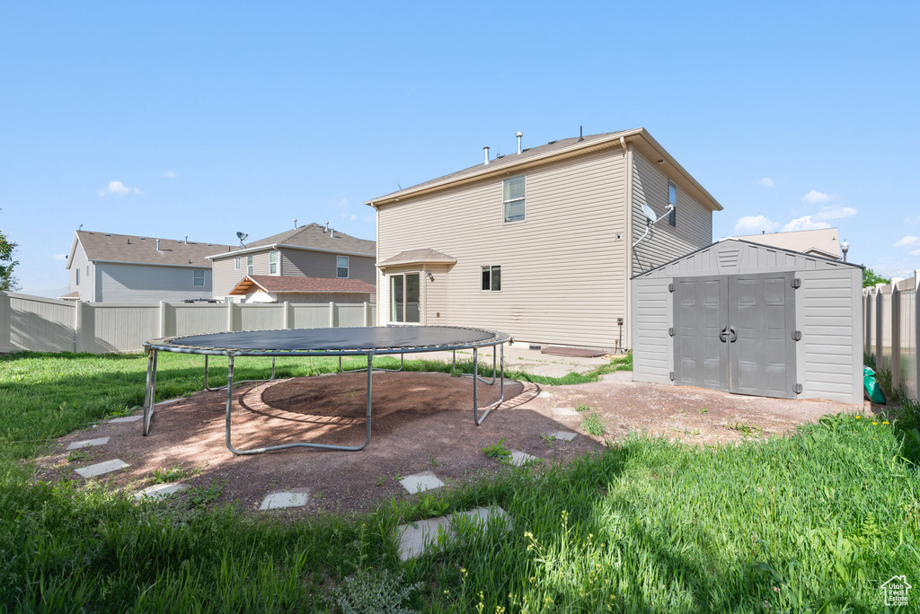 Back of house featuring a trampoline, a storage unit, an outbuilding, and a fenced backyard