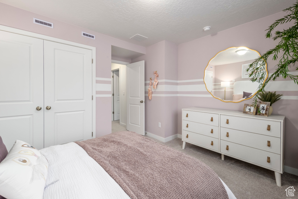 Bedroom featuring light colored carpet, a textured ceiling, a closet, and baseboards