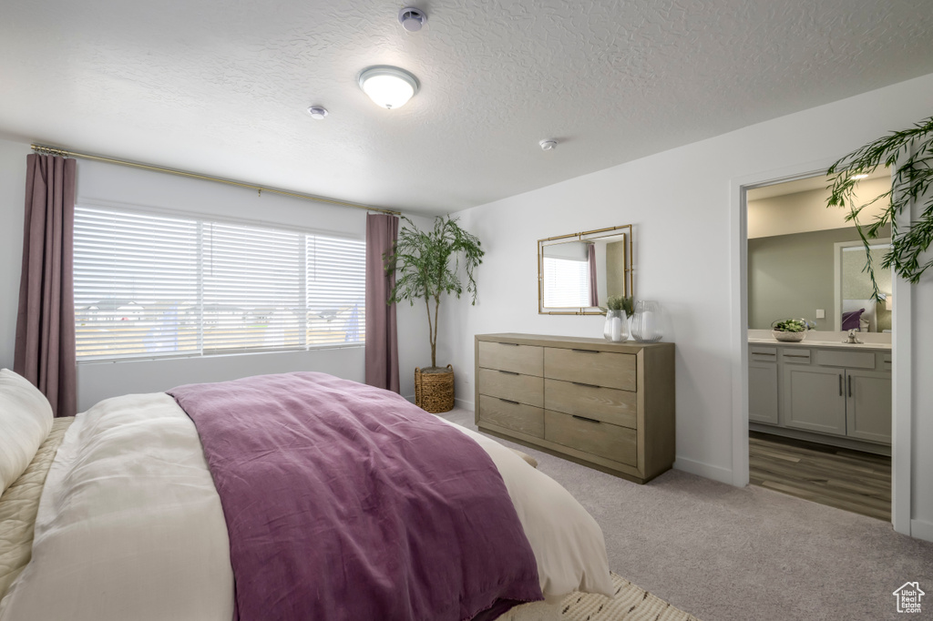 Bedroom with carpet floors, a textured ceiling, ensuite bathroom, and a sink