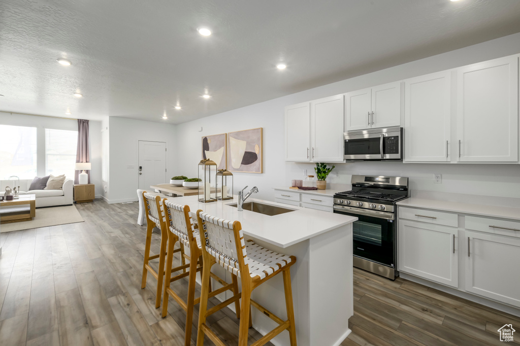Kitchen featuring stainless steel appliances, a sink, dark wood finished floors, a kitchen breakfast bar, and white cabinetry
