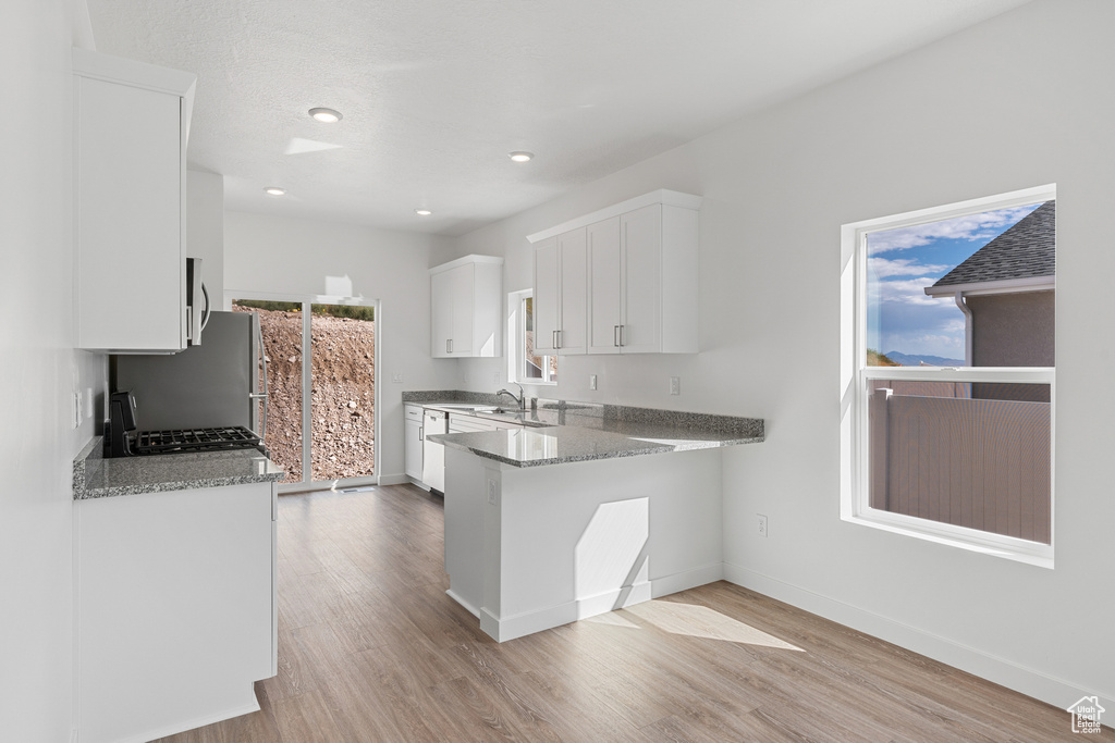 Kitchen featuring light wood-type flooring, white cabinetry, baseboards, freestanding refrigerator, and a sink