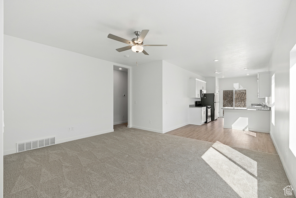 Unfurnished living room featuring light colored carpet, ceiling fan, baseboards, and recessed lighting