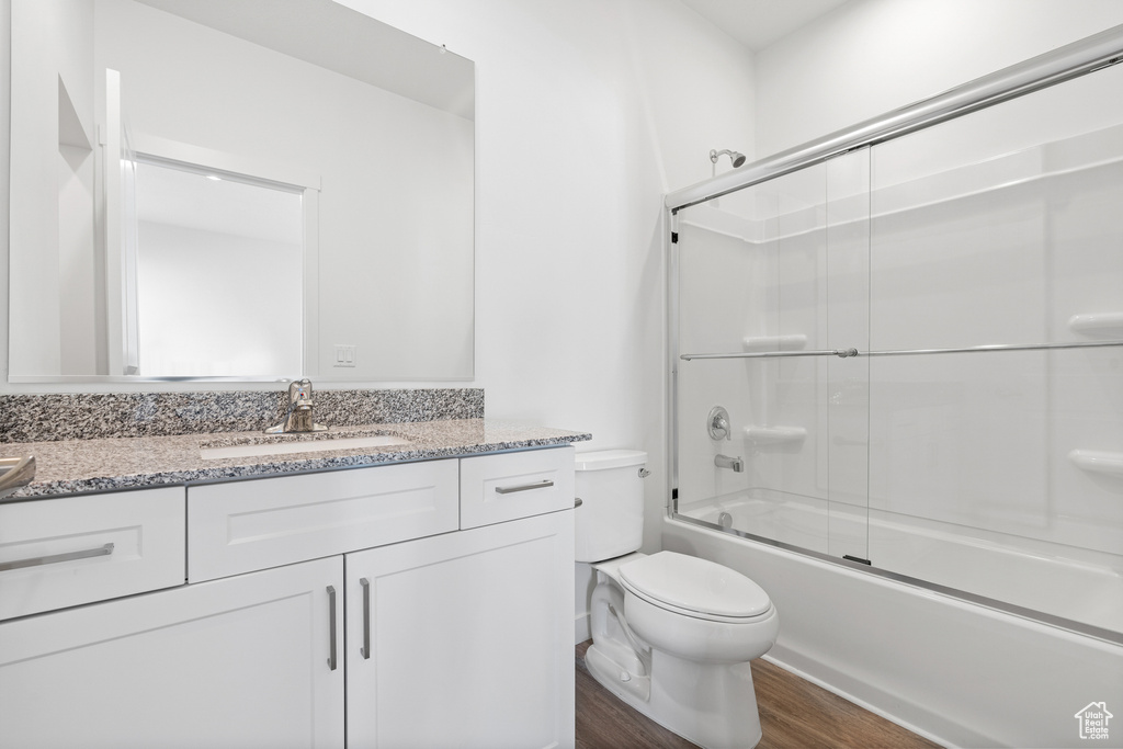 Full bathroom with wood finished floors, vanity, toilet, and bath / shower combo with glass door
