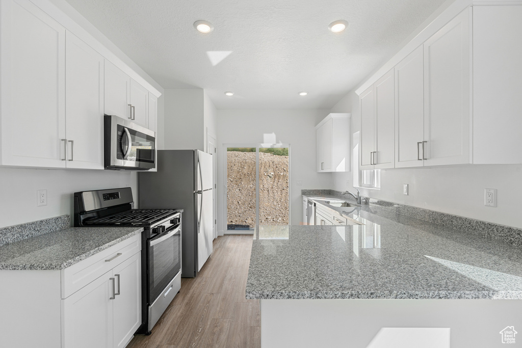 Kitchen with appliances with stainless steel finishes, light stone counters, white cabinets, recessed lighting, and a peninsula