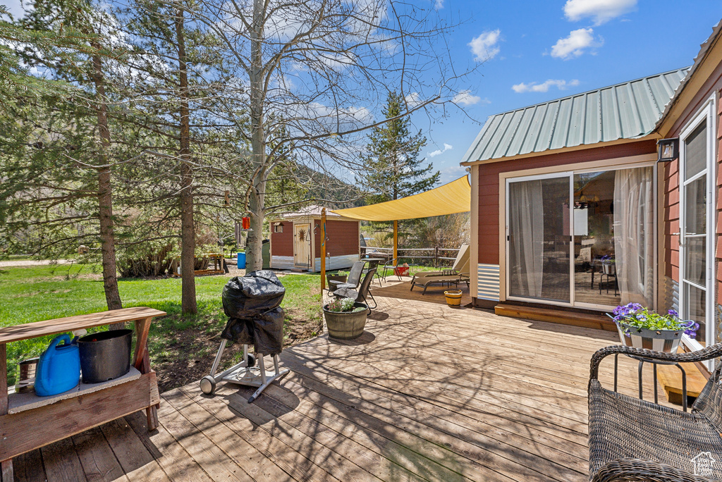 Wooden terrace featuring an outbuilding, a storage unit, a lawn, and grilling area