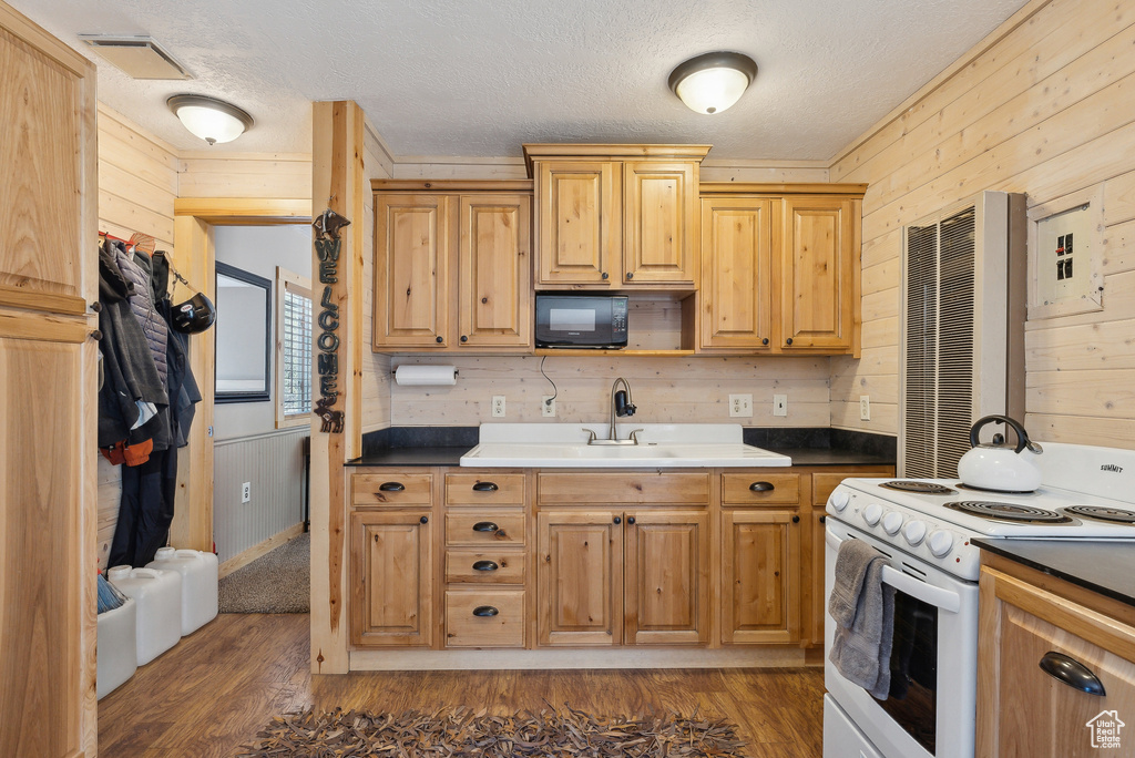 Kitchen with electric stove, black microwave, wood walls, dark wood-style flooring, and a textured ceiling