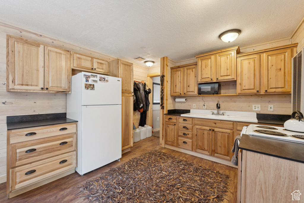 Kitchen featuring white appliances, dark wood finished floors, light brown cabinets, dark countertops, and a sink