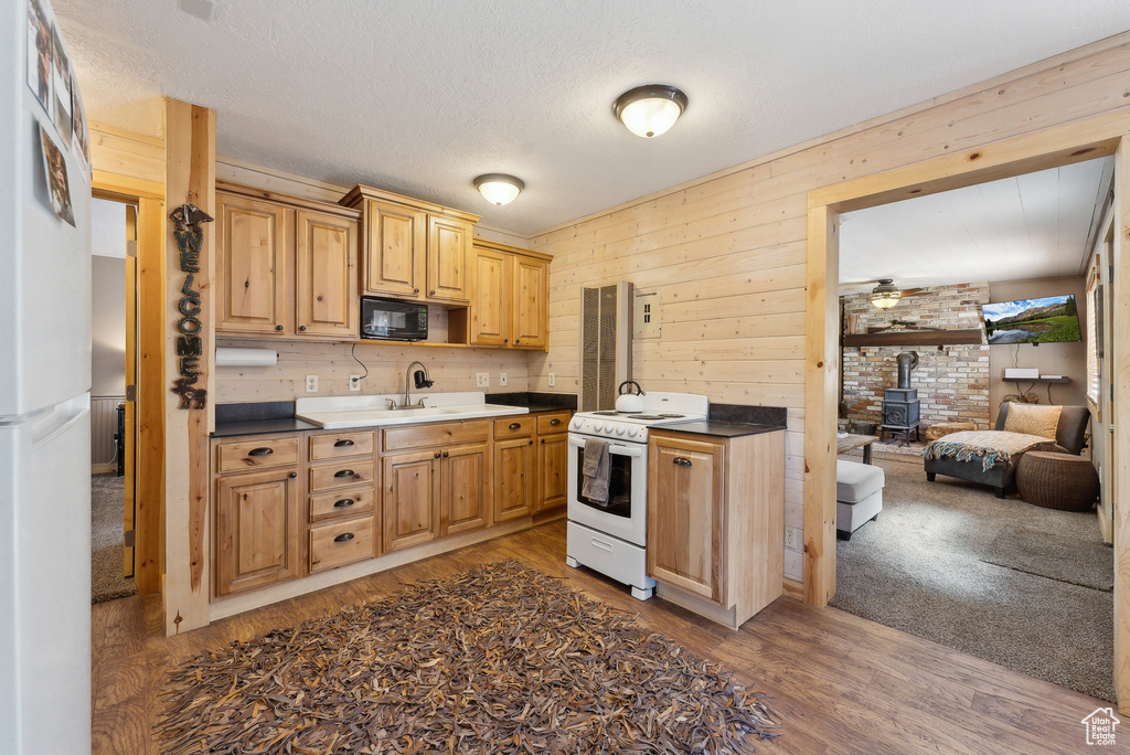 Kitchen with electric range, a wood stove, black microwave, wood finished floors, and a sink