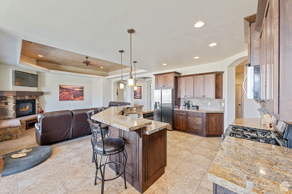Kitchen with arched walkways, appliances with stainless steel finishes, a fireplace, a kitchen bar, and open floor plan
