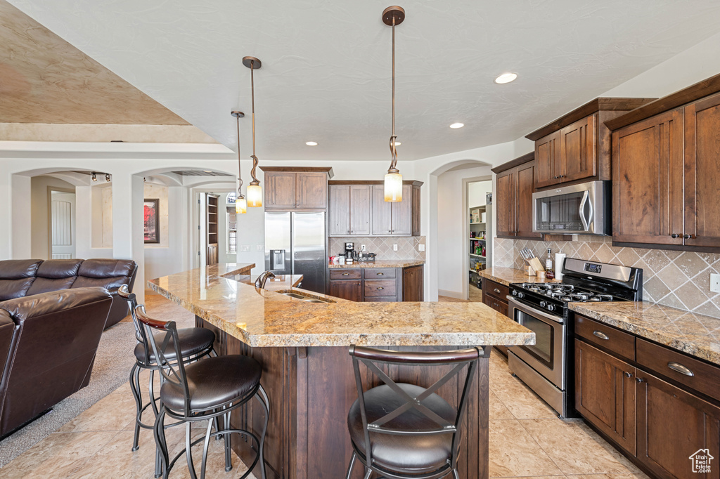 Kitchen featuring stainless steel appliances, arched walkways, a sink, open floor plan, and a breakfast bar