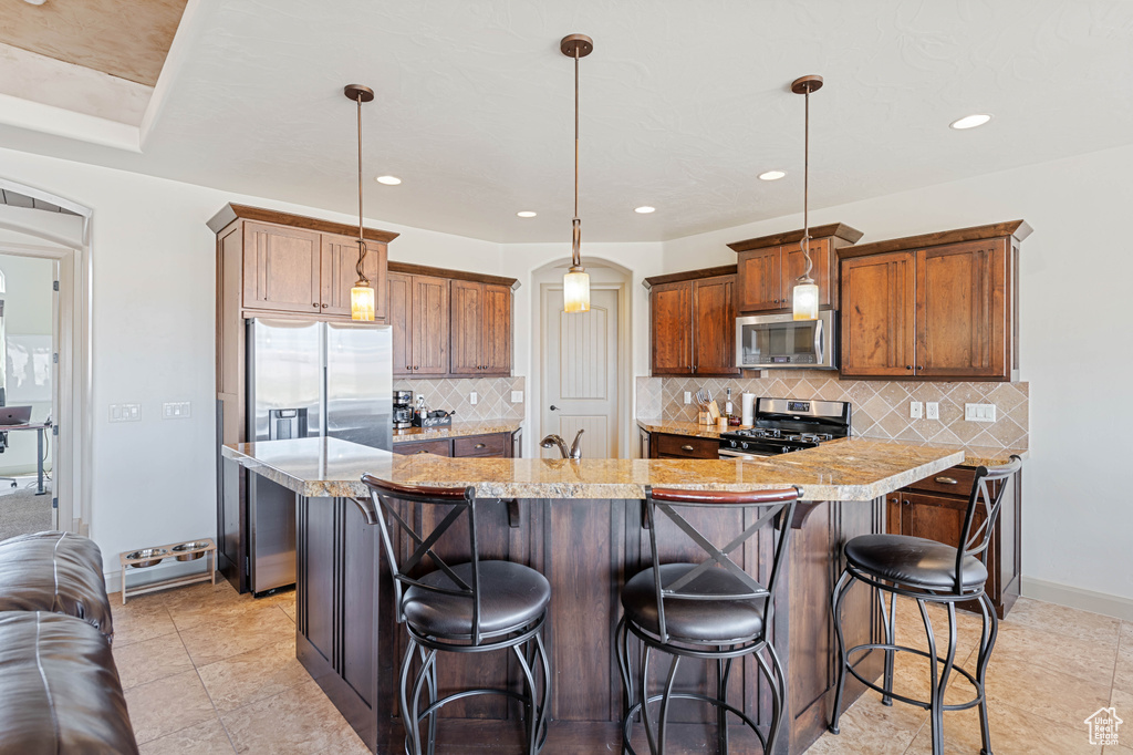 Kitchen with stainless steel appliances, arched walkways, tasteful backsplash, a breakfast bar area, and a large island