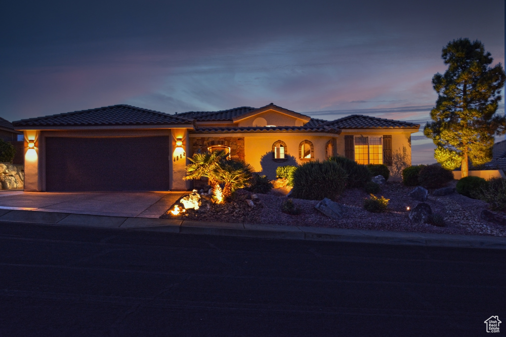 View of front facade featuring a tiled roof, a garage, stucco siding, and concrete driveway