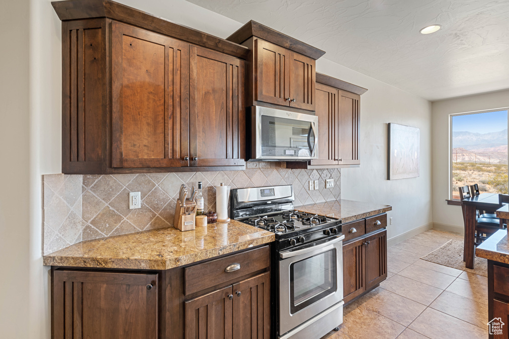 Kitchen featuring stainless steel appliances, decorative backsplash, baseboards, light tile patterned floors, and light stone counters