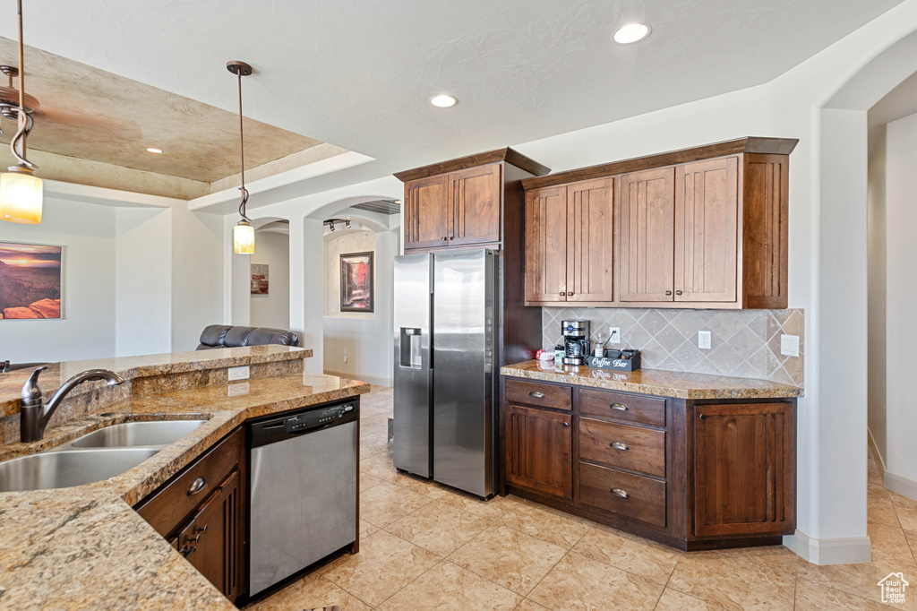 Kitchen featuring stainless steel appliances, a sink, arched walkways, backsplash, and hanging light fixtures