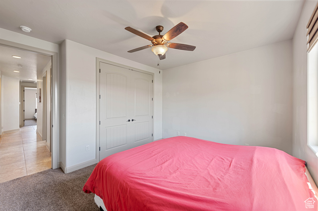 Bedroom featuring a closet, light colored carpet, light tile patterned floors, a ceiling fan, and baseboards