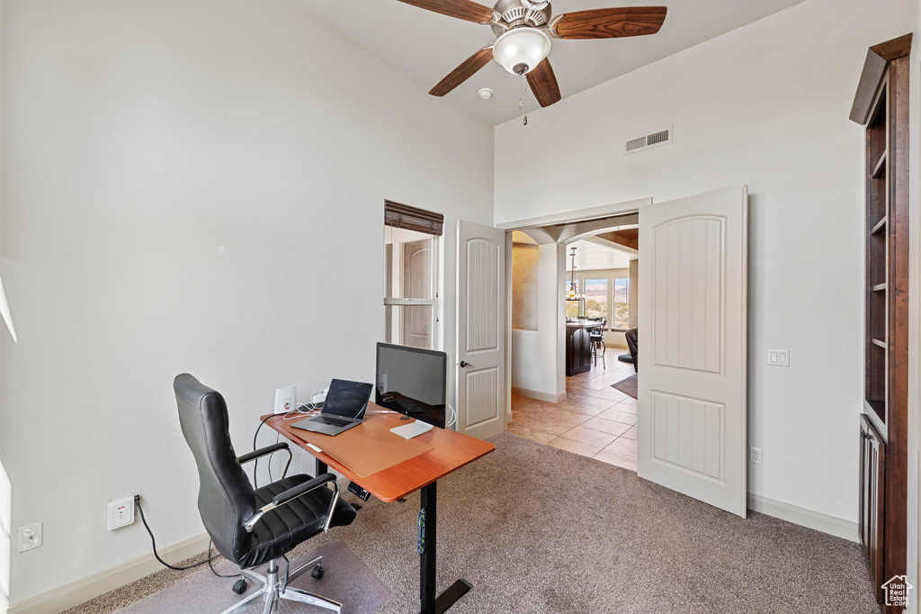 Office space featuring ceiling fan, light carpet, baseboards, light tile patterned floors, and a high ceiling