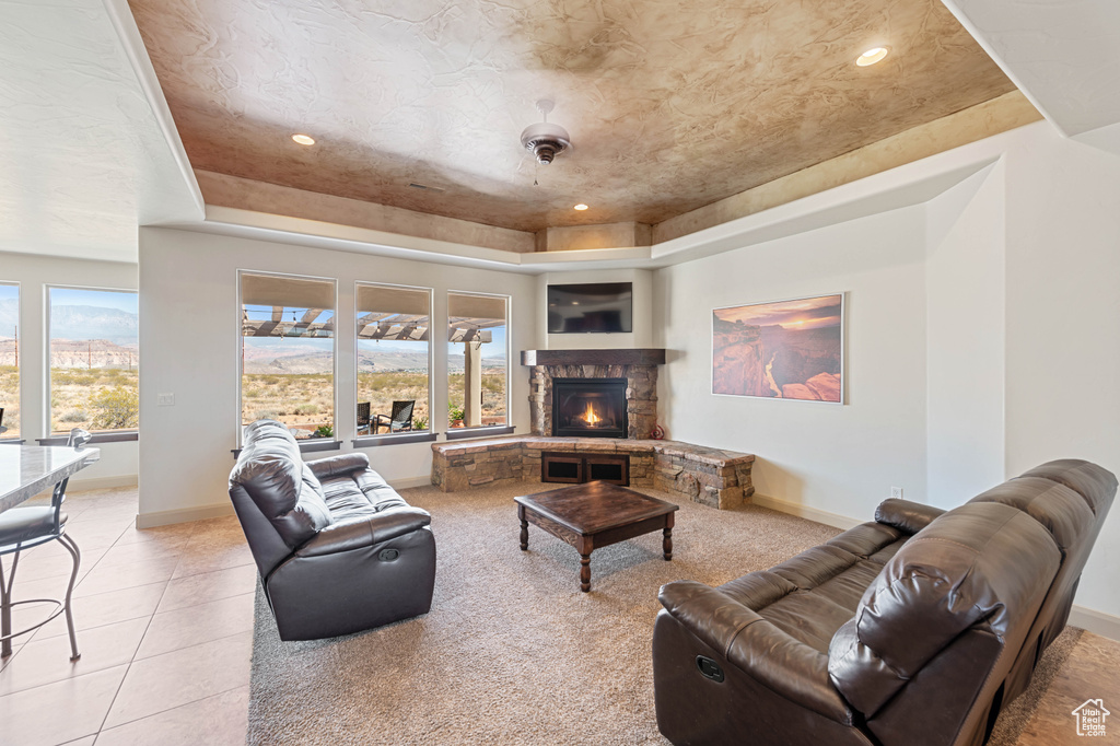 Living area with a tray ceiling, a stone fireplace, baseboards, light tile patterned floors, and recessed lighting