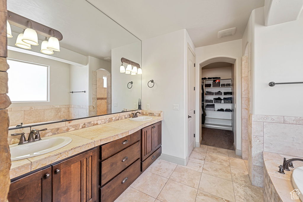 Bathroom featuring double vanity, tile patterned flooring, tiled tub, and a spacious closet