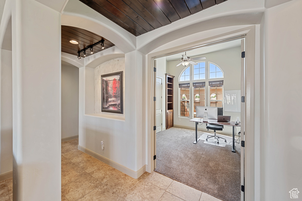 Corridor with baseboards, a desk, wood ceiling, tile patterned floors, and arched walkways