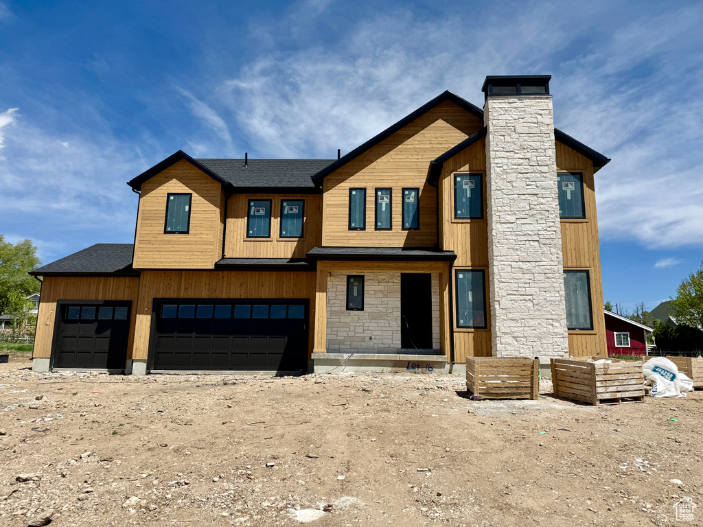 Contemporary house featuring a garage, stone siding, roof with shingles, and a chimney
