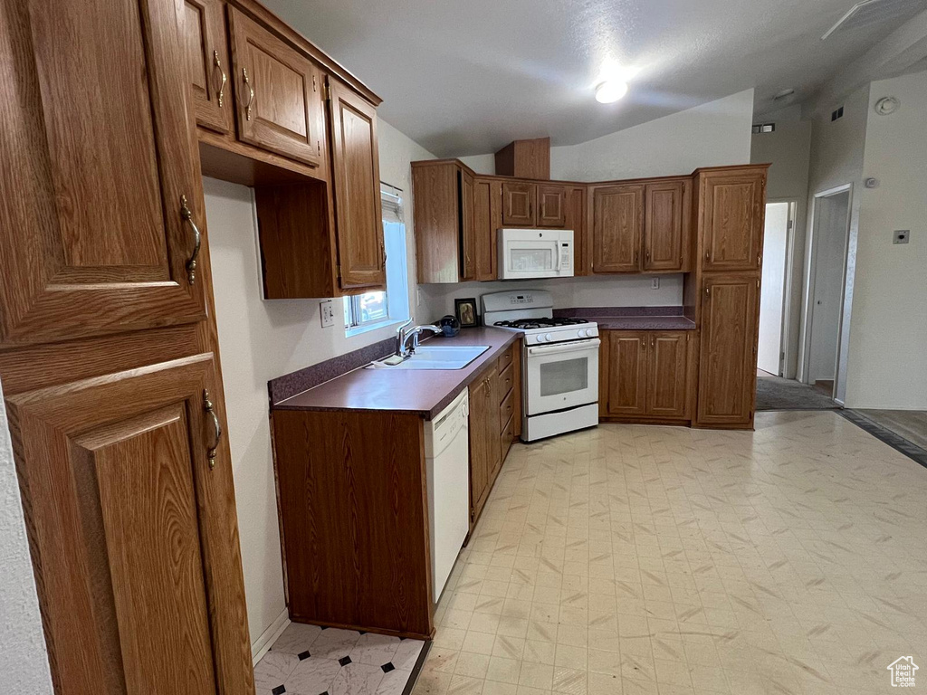 Kitchen with white appliances, a sink, vaulted ceiling, dark countertops, and light floors