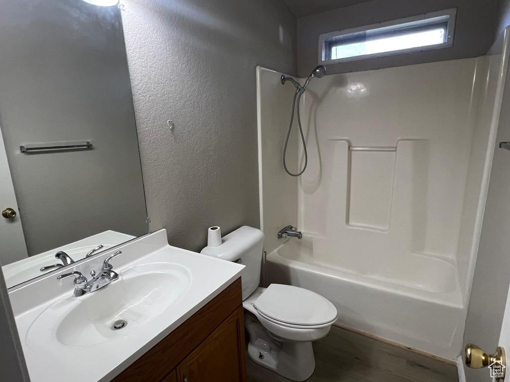 Bathroom with toilet, vanity, tub / shower combination, wood finished floors, and a textured wall