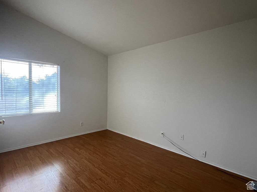 Empty room featuring wood finished floors, vaulted ceiling, and baseboards