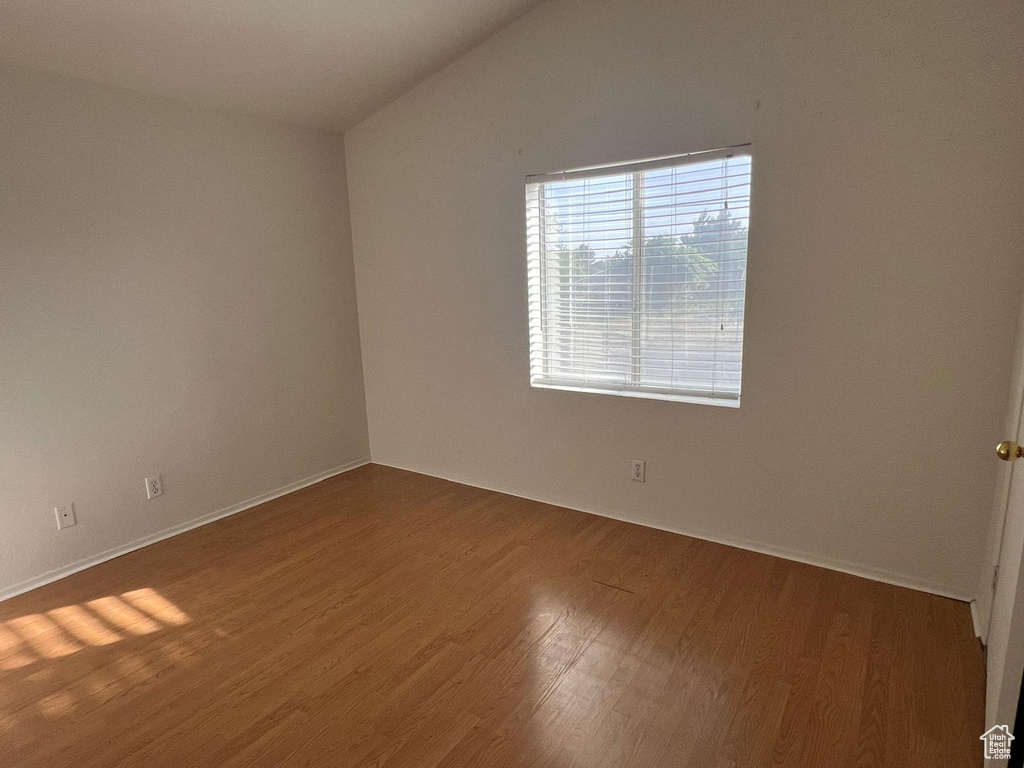 Unfurnished room with wood finished floors, lofted ceiling, and baseboards