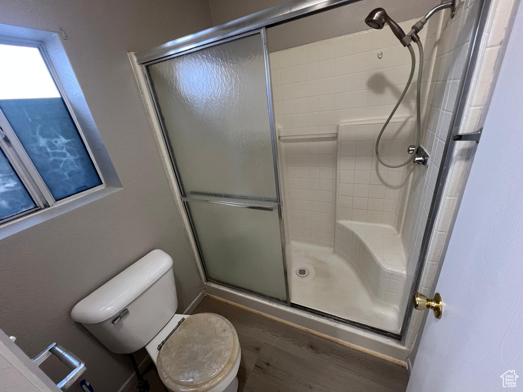 Full bathroom with a shower stall, wood finished floors, and toilet