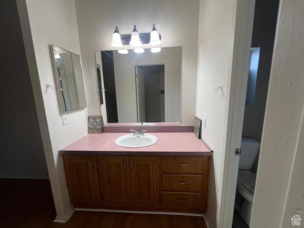Bathroom with toilet, wood finished floors, vanity, and a textured wall