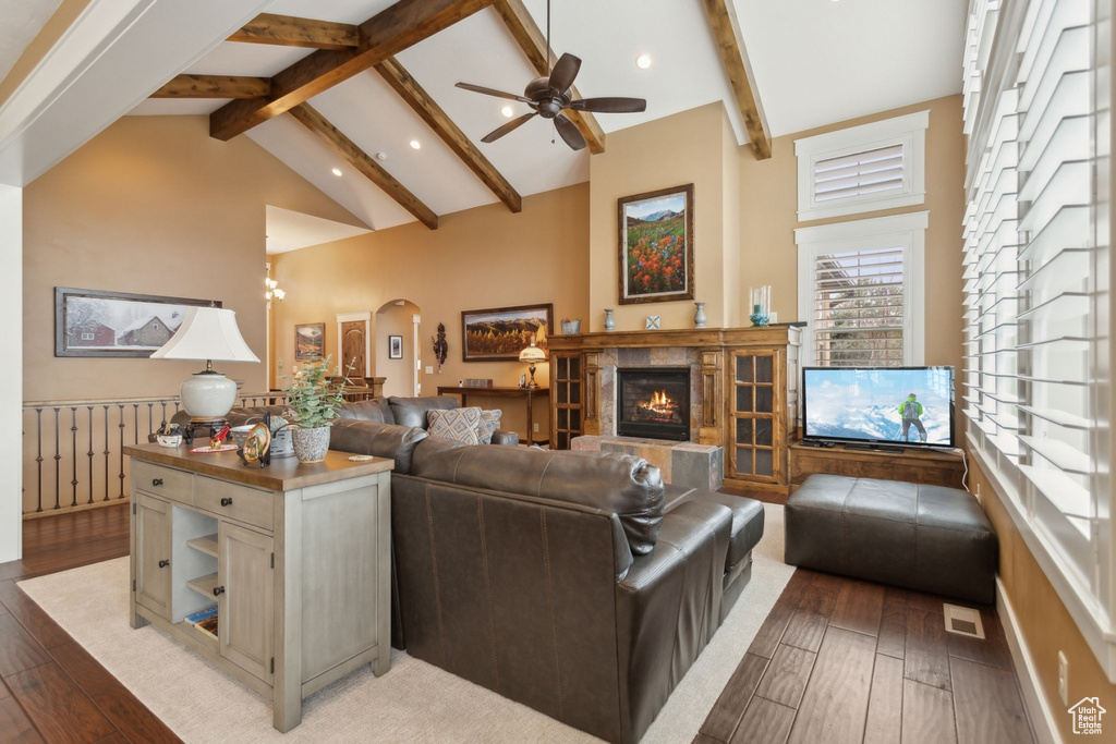 Living area featuring beamed ceiling, a tiled fireplace, light wood finished floors, a ceiling fan, and high vaulted ceiling