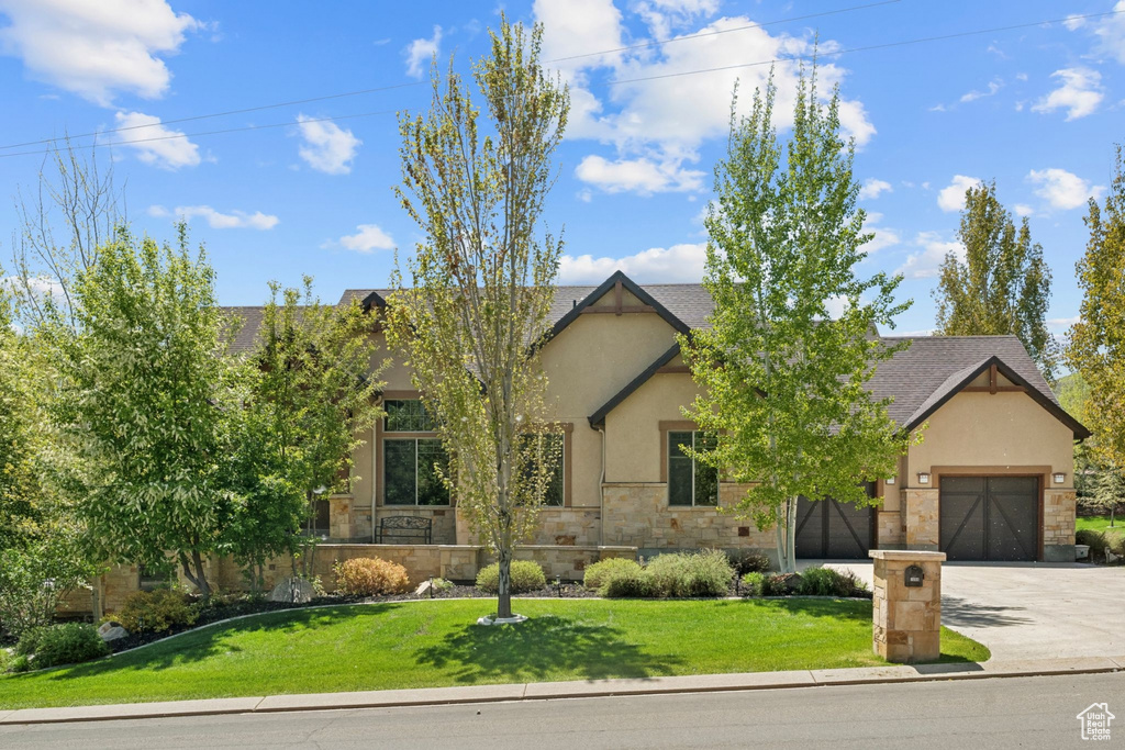 View of front facade with stone siding, concrete driveway, an attached garage, a front yard, and stucco siding