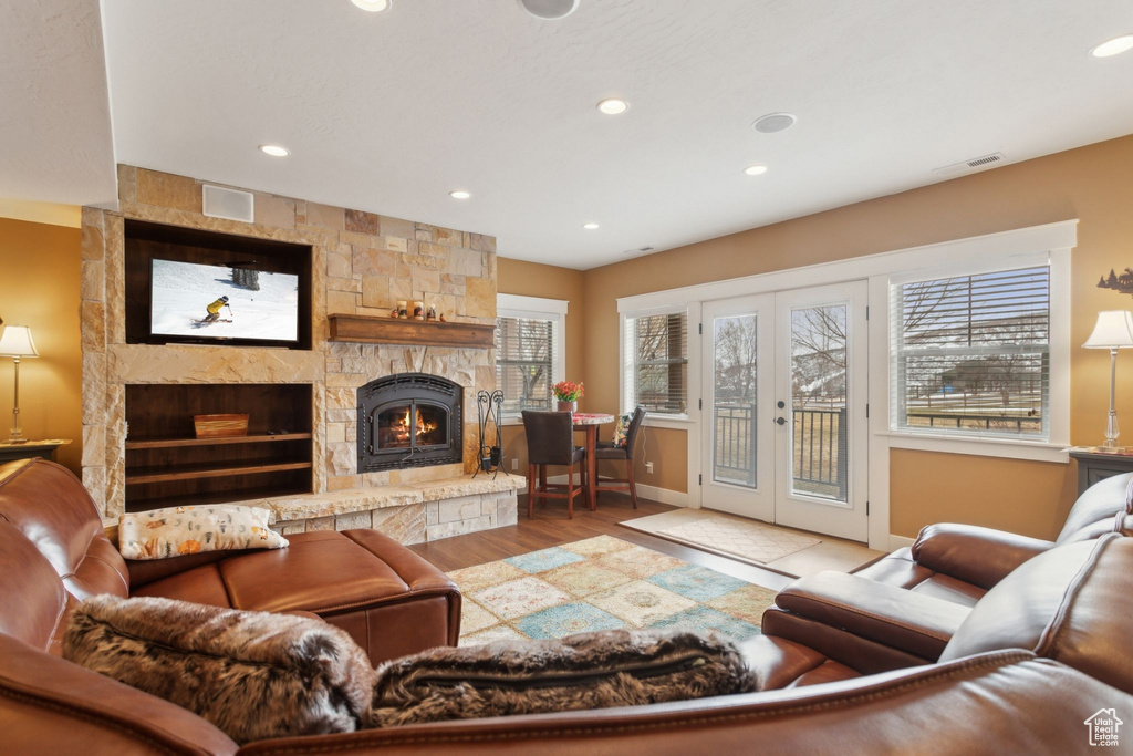 Living room with a stone fireplace, french doors, recessed lighting, baseboards, and wood finished floors