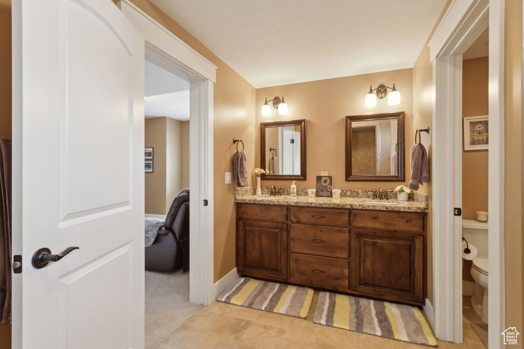 Full bath with toilet, double vanity, ensuite bath, and baseboards