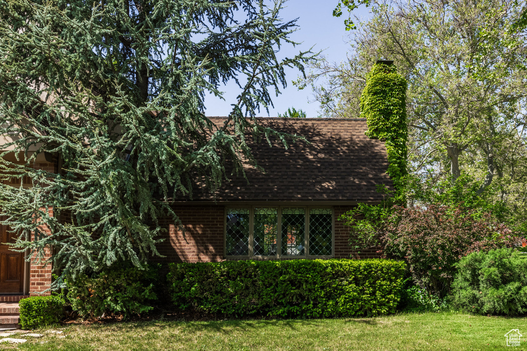 View of front of house with brick siding, a shingled roof, a front lawn, and a chimney
