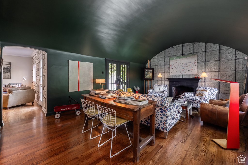 Dining space featuring wood finished floors, arched walkways, baseboards, lofted ceiling, and a large fireplace