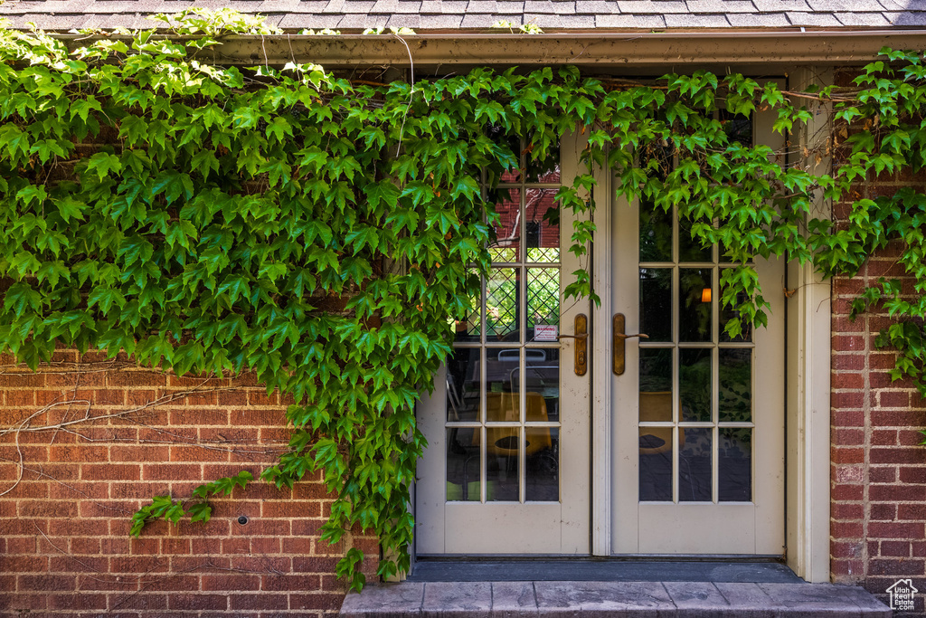 View of exterior entry featuring french doors, a shingled roof, and brick siding