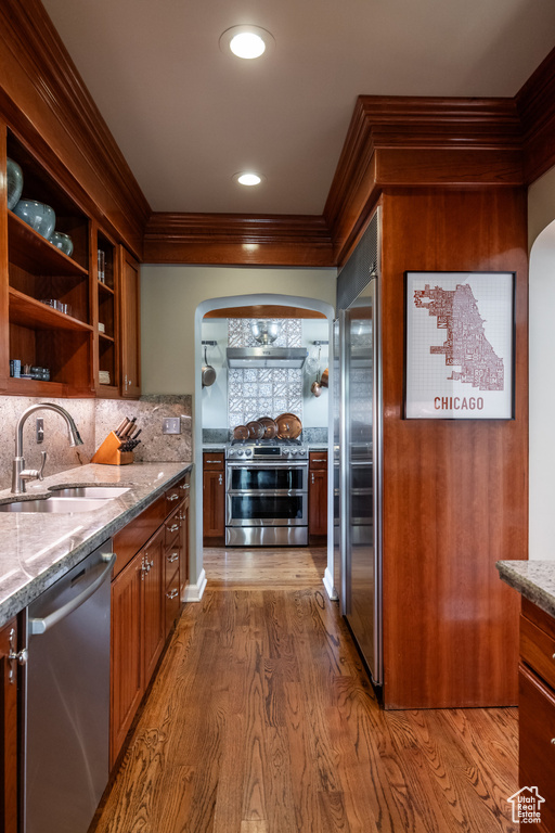 Kitchen featuring stainless steel appliances, a sink, arched walkways, ornamental molding, and light stone countertops