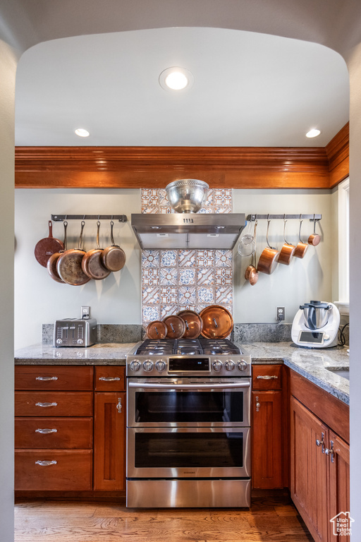 Kitchen featuring range with two ovens, light wood finished floors, brown cabinetry, recessed lighting, and light stone countertops