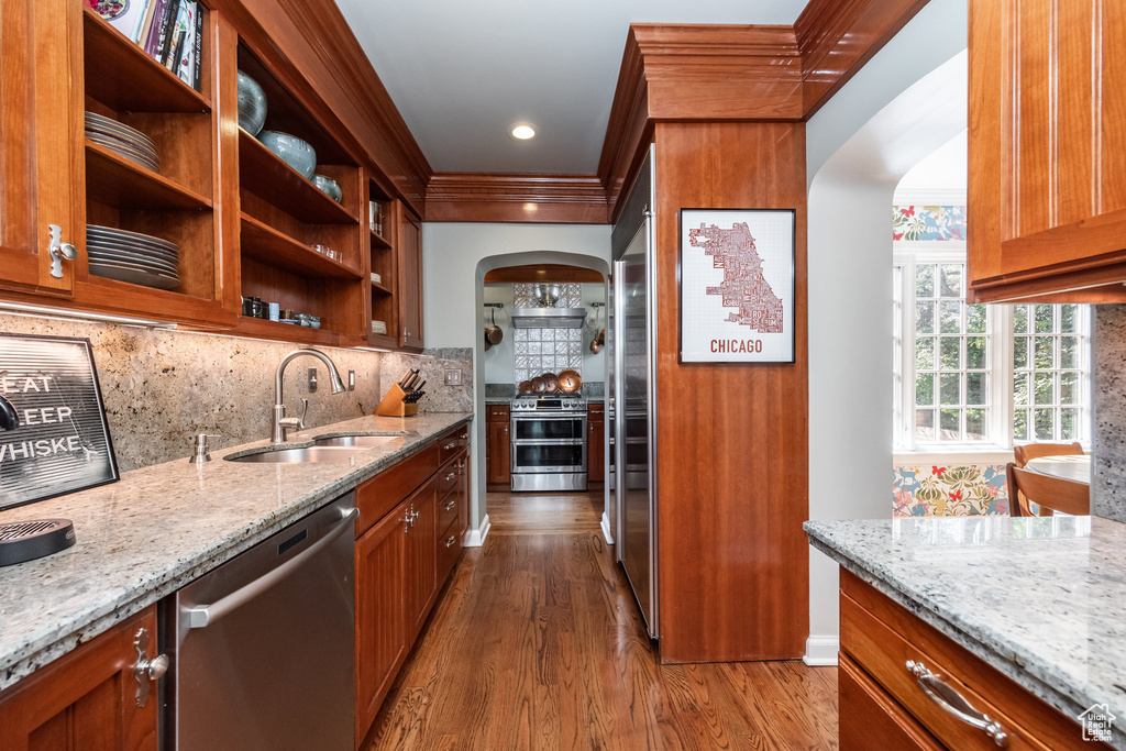 Kitchen with stainless steel appliances, a sink, arched walkways, dark wood-style floors, and light stone countertops