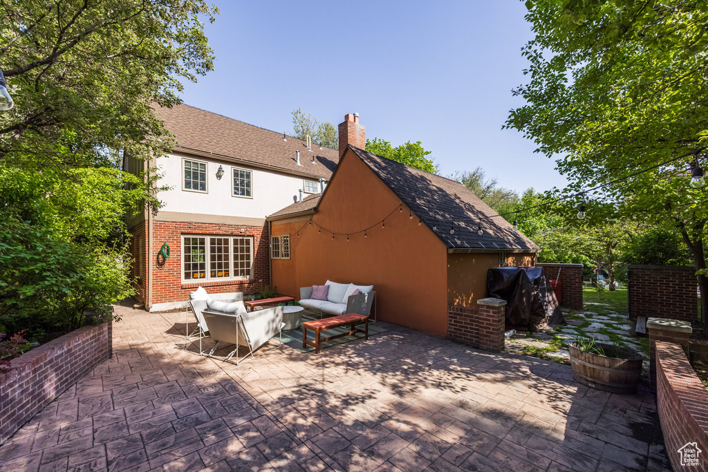Back of property featuring an outdoor living space, a patio, a chimney, stucco siding, and brick siding