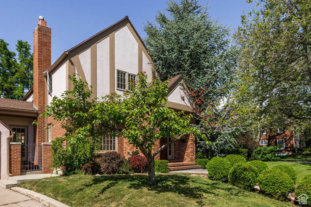 Tudor house featuring a chimney, brick siding, stucco siding, and a front yard