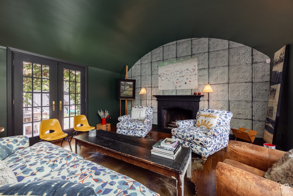 Living room with lofted ceiling, french doors, a tiled fireplace, and wood finished floors